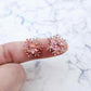 One pair of 16mm holographic rose gold glitter acrylic snowflake stud earring blanks shown on a finger for size reference.