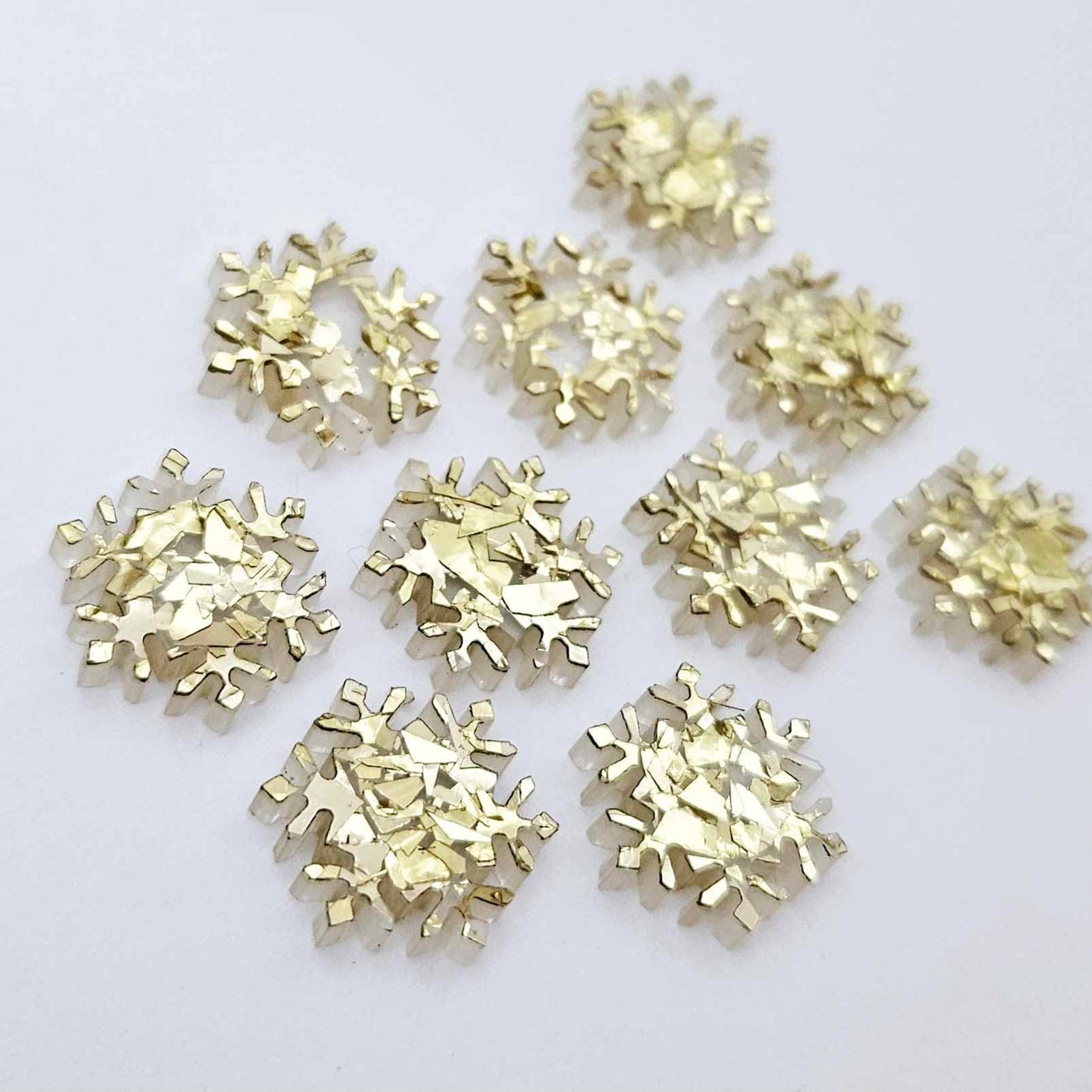 Five pairs of 16mm chunky gold glitter acrylic snowflake stud earring blanks laying flat.