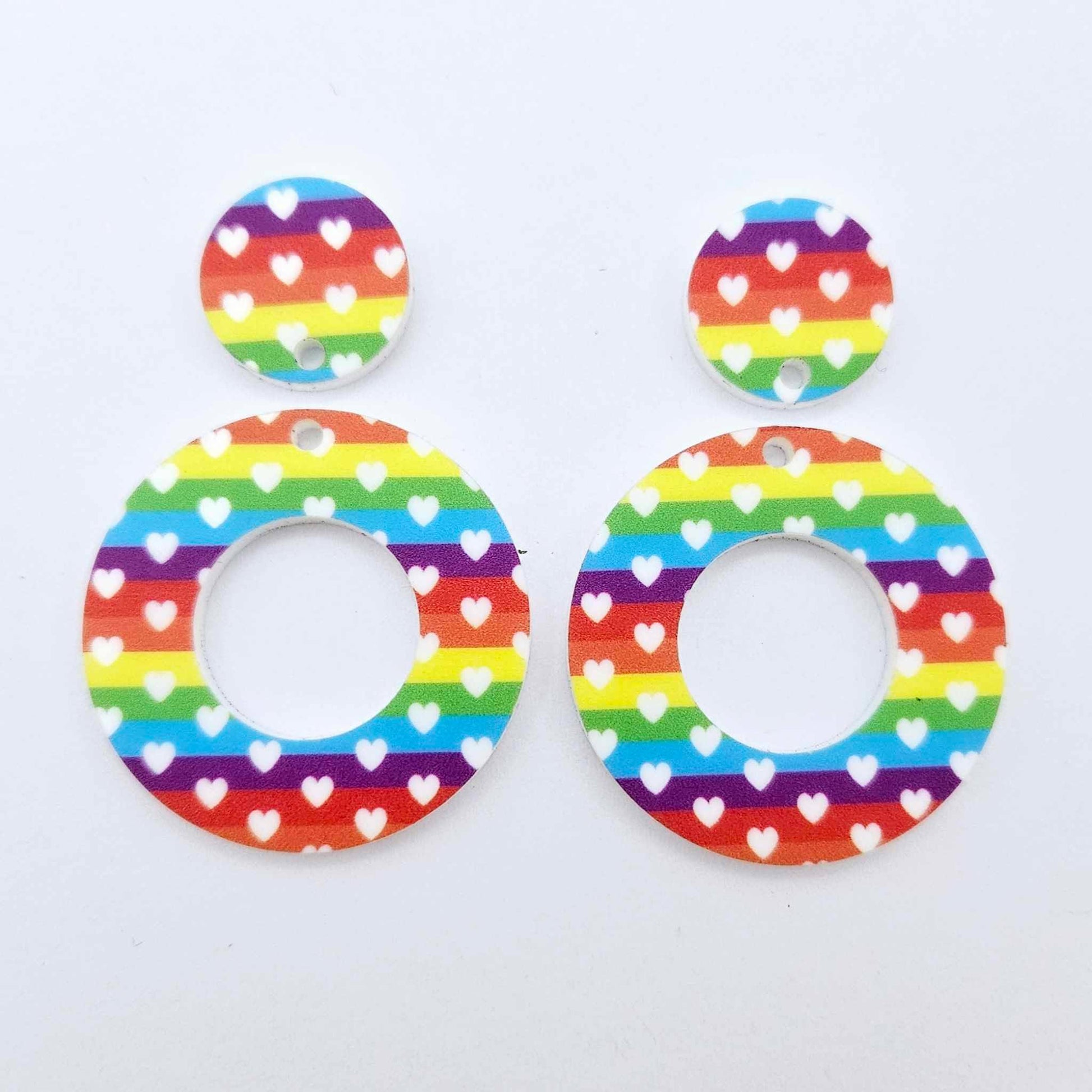 One pair of 33mm Rainbow Love UV printed acrylic mini hoop dangle blanks featuring a colourful rainbow and white heart print with matching toppers laying flat.