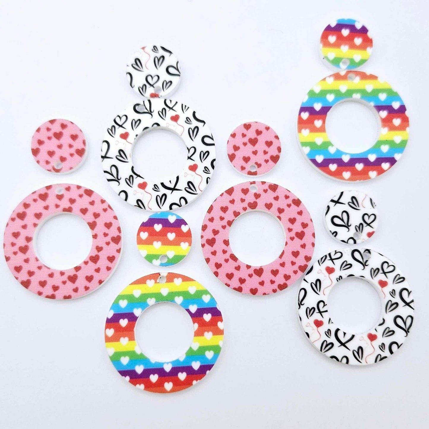Three pairs of 33mm Love is Love UV printed acrylic mini hoop dangle earring blanks with matching toppers in Rainbow Love, Pink & Red Hearts and Red & Black Hearts designs laying flat.