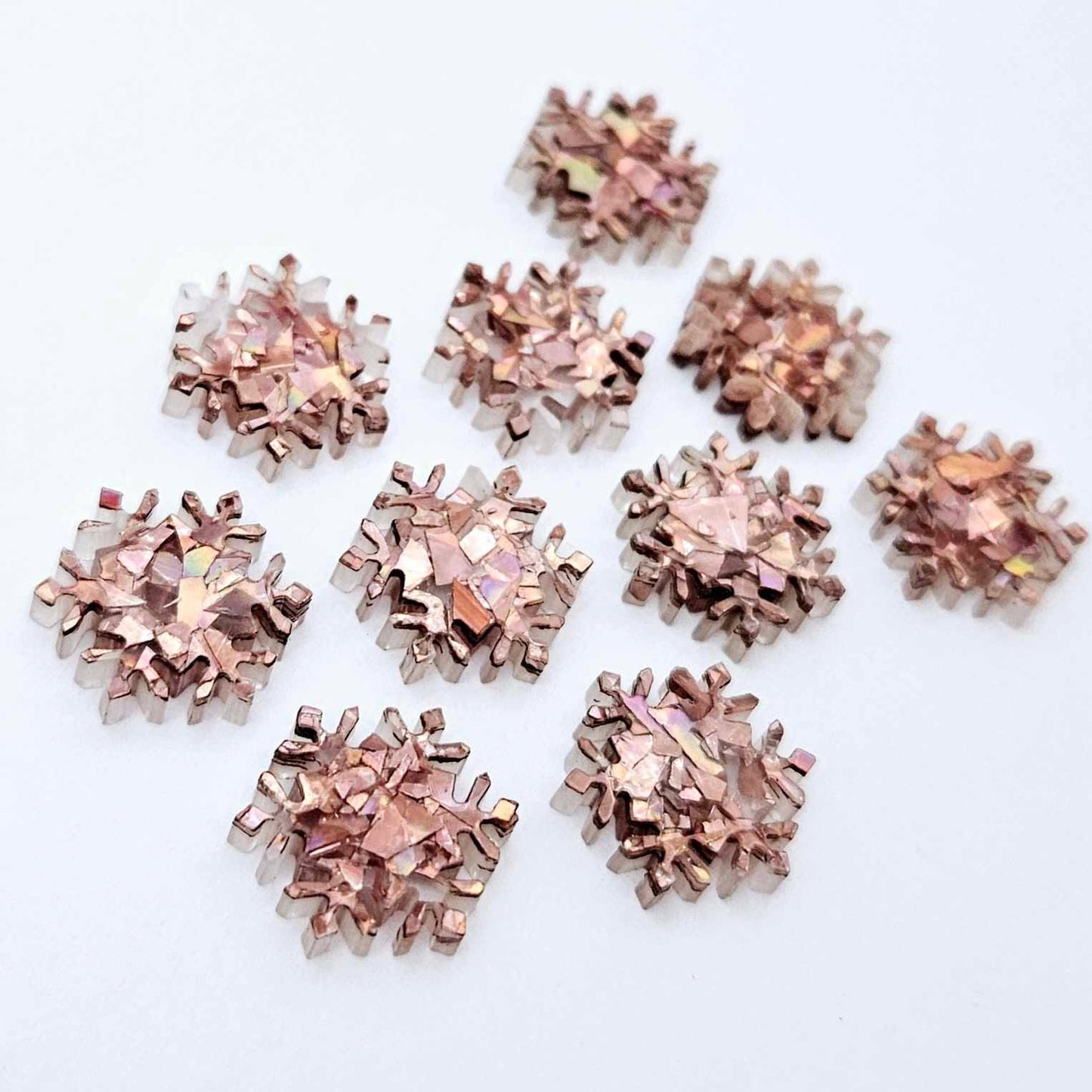 Five pairs of 16mm chunky rose gold glitter acrylic snowflake stud earring blanks laying flat.