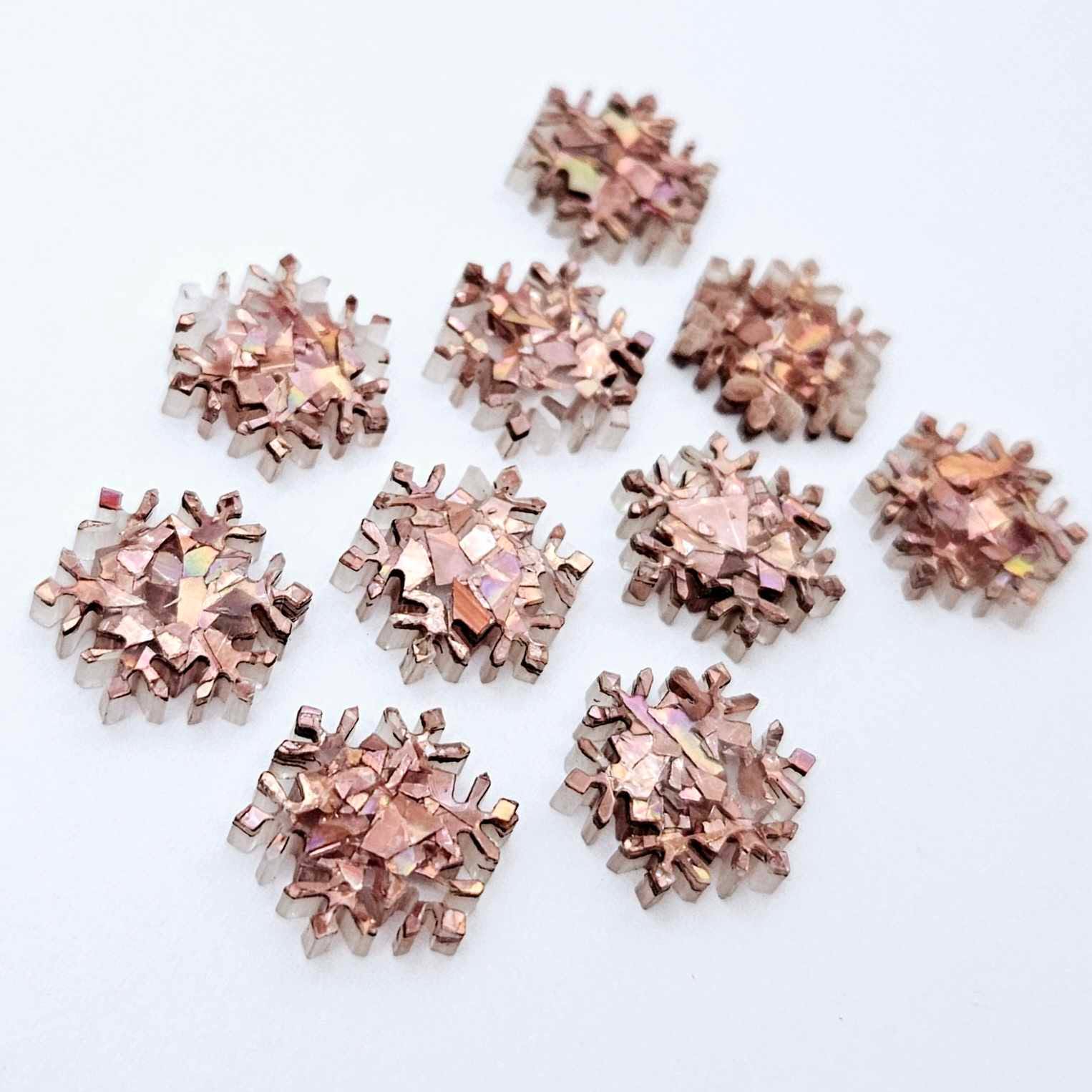 Five pairs of 16mm chunky rose gold glitter acrylic snowflake stud earring blanks laying flat.