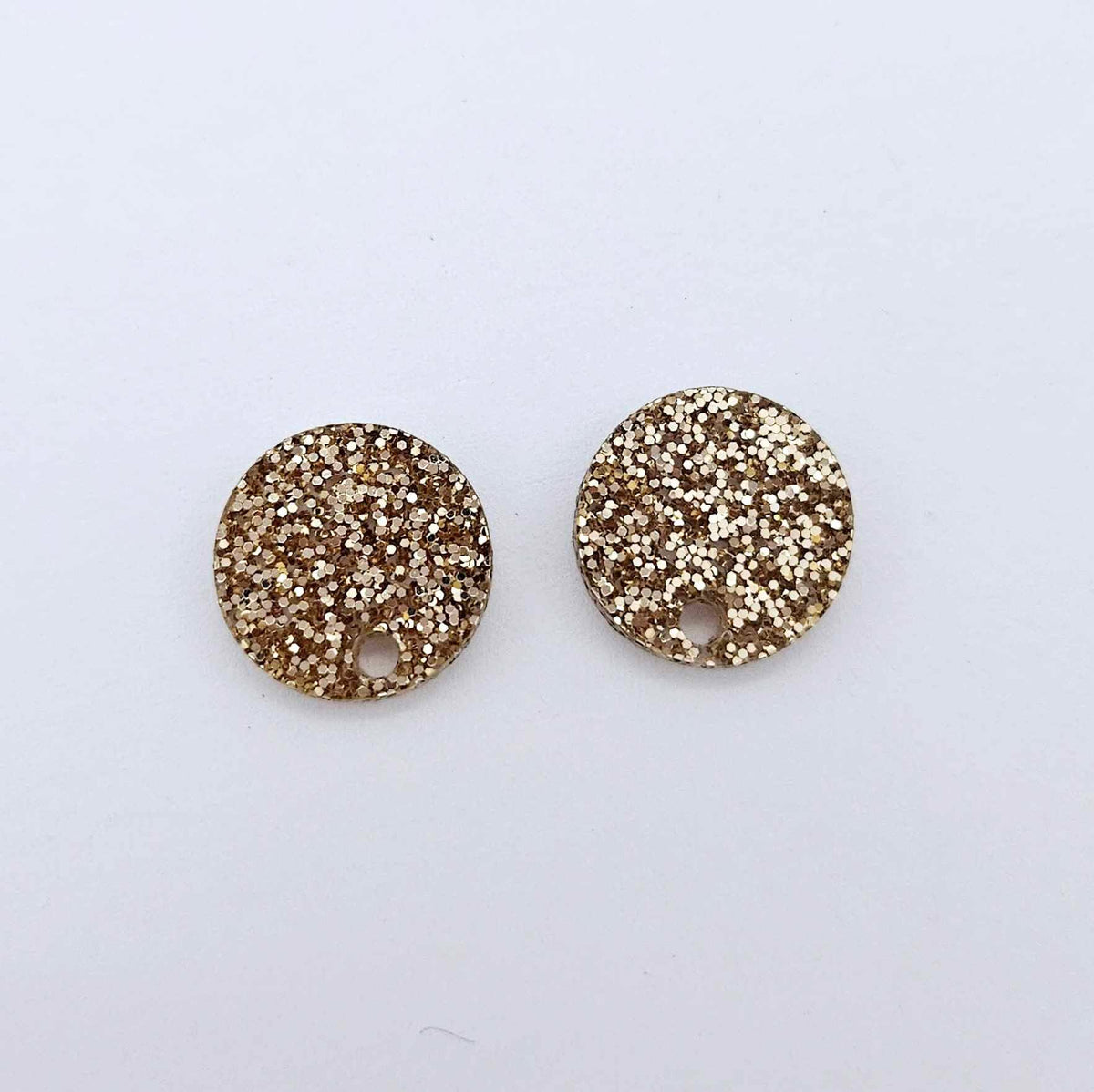 One pair of 14mm fine rose gold glitter acrylic circle earring toppers laying flat.