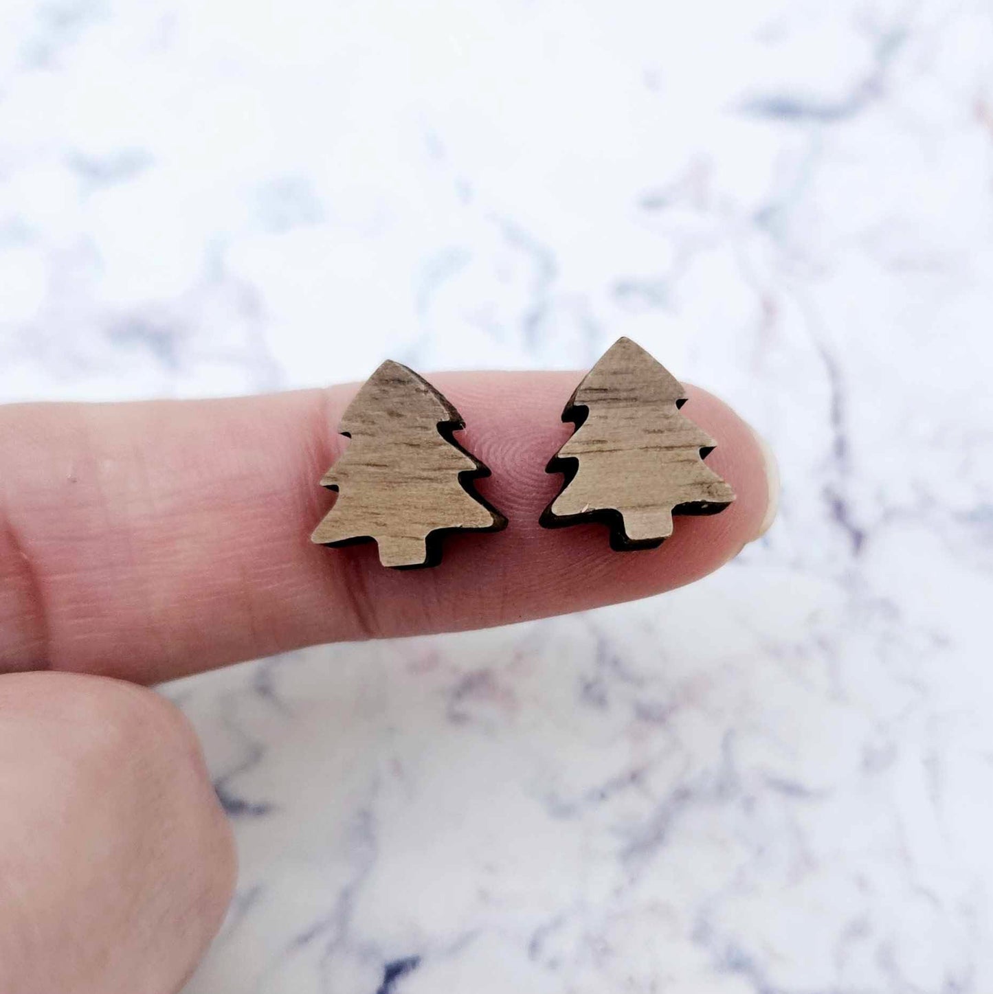 One pair of 12mm walnut veneer Christmas tree stud earring blanks shown on a finger for size reference.