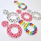 Three pairs of 33mm Love is Love UV printed acrylic mini hoop dangle earring blanks with matching toppers in Rainbow Love, Pink & Red Hearts and Red & Black Hearts designs laying flat.