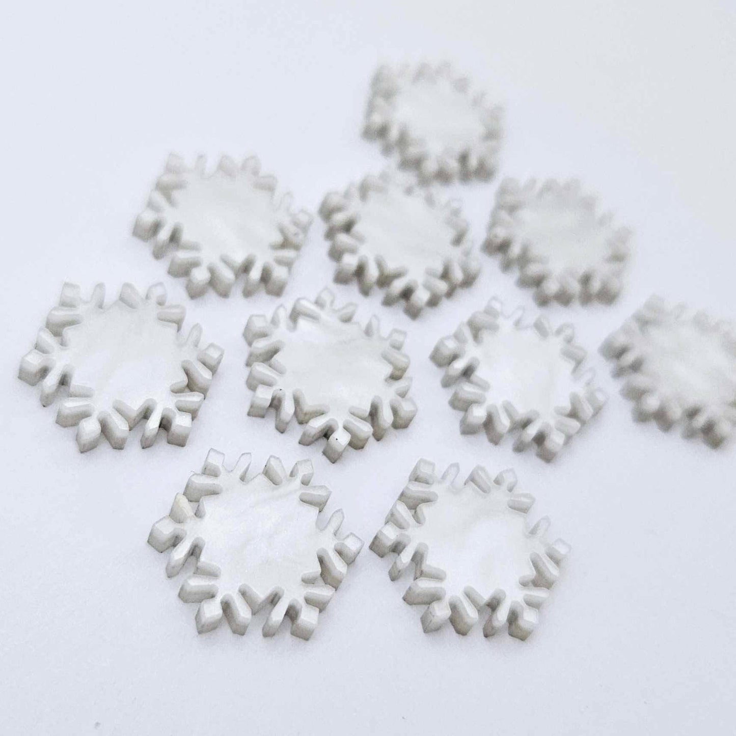 Five pairs of 16mm white marble acrylic snowflake stud earring blanks laying flat.