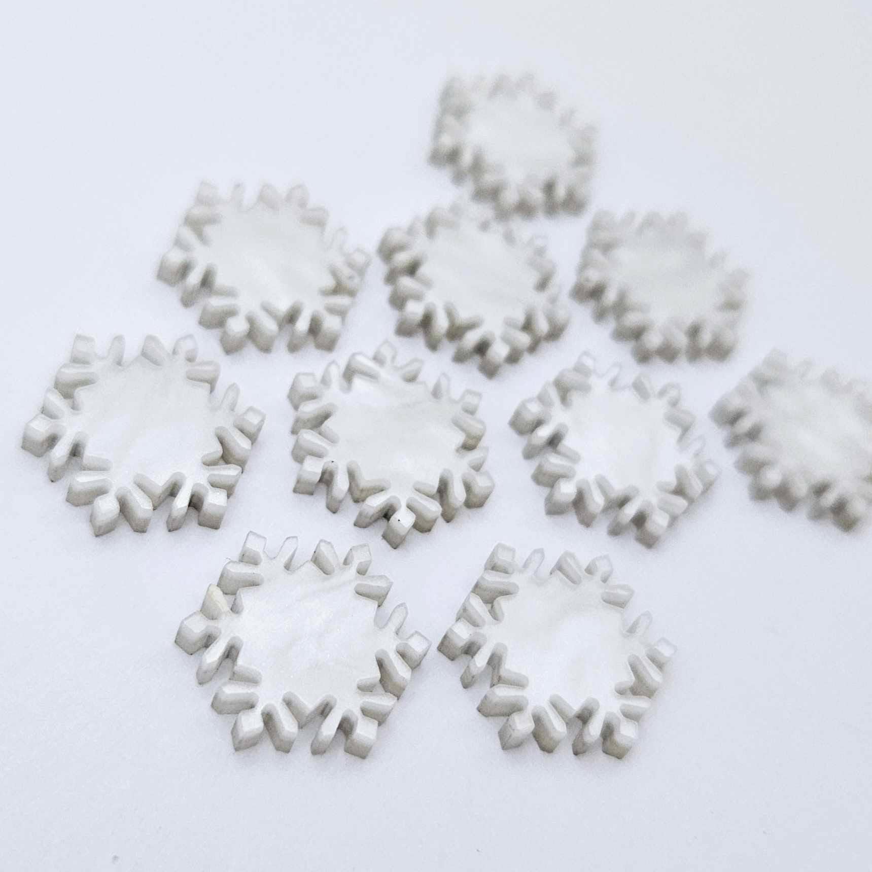 Five pairs of 16mm white marble acrylic snowflake stud earring blanks laying flat.