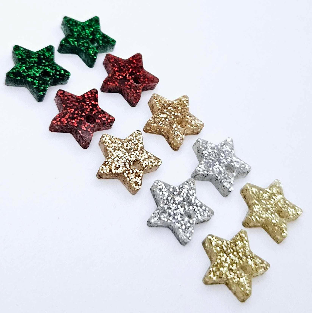 A selection of 14mm fine glitter acrylic star earring toppers in gold, silver, green, red and rose gold glitter laying flat