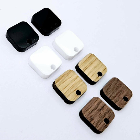 12mm rounded square earring toppers in walnut, oak, white and black, with one pair of each finish laid flat together.