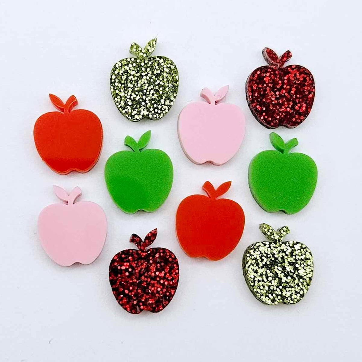 14mm apple acrylic earring stud blanks in red, lime green, pastel pink, red glitter and light green glitter laid flat together.