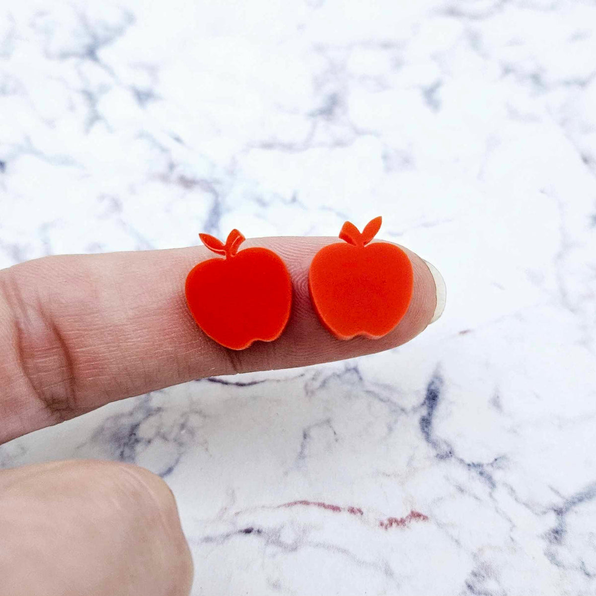 14mm solid red acrylic apple stud earring blanks shown on a finger for size reference.