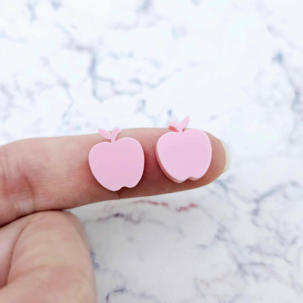 14mm pastel pink acrylic apple stud earring blanks shown on a finger for size reference.