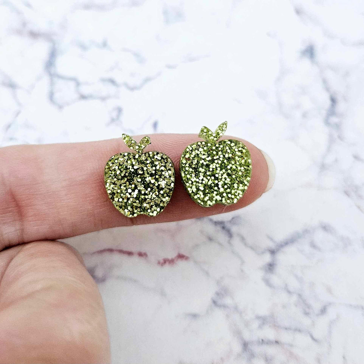 14mm lime green glitter acrylic apple stud earring blanks shown on a finger for size reference.