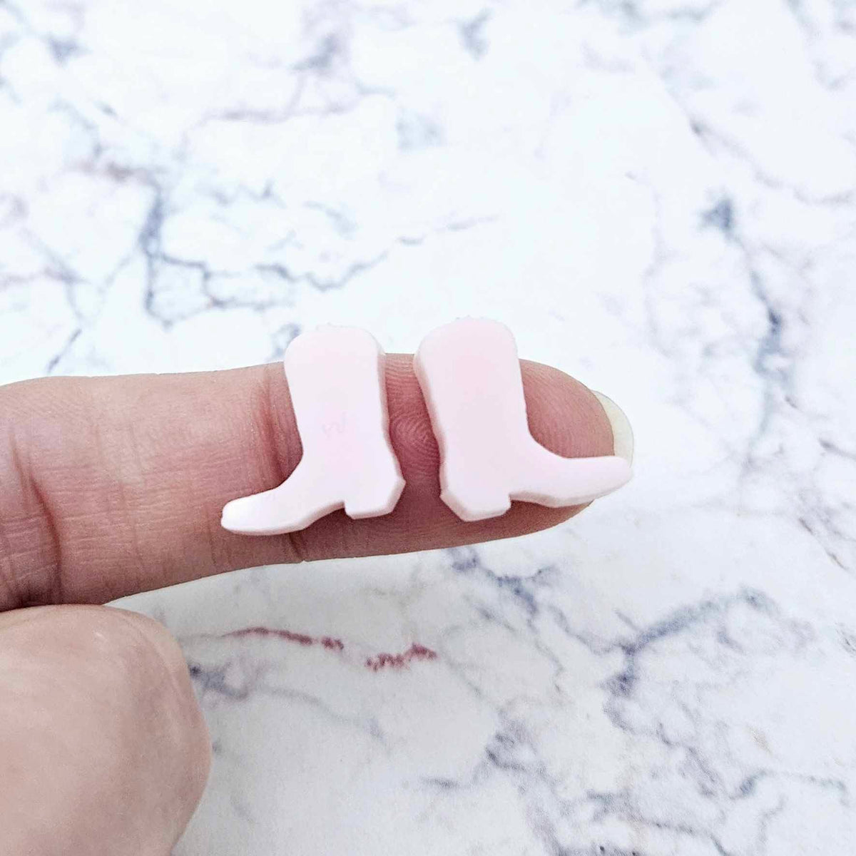 One pair of 15mm strawberry milkshake pink acrylic boot stud earring blanks shown on a finger for size reference.