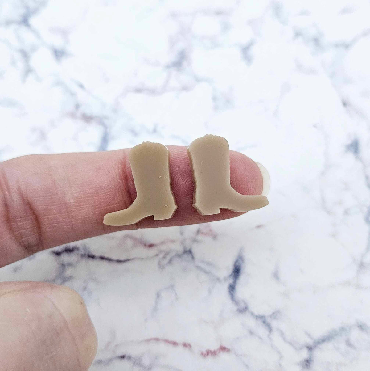 One pair of 15mm iced coffee acrylic boot stud earring blanks shown on a finger for size reference.