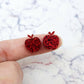 14mm red glitter acrylic apple stud earring blanks shown on a finger for size reference.