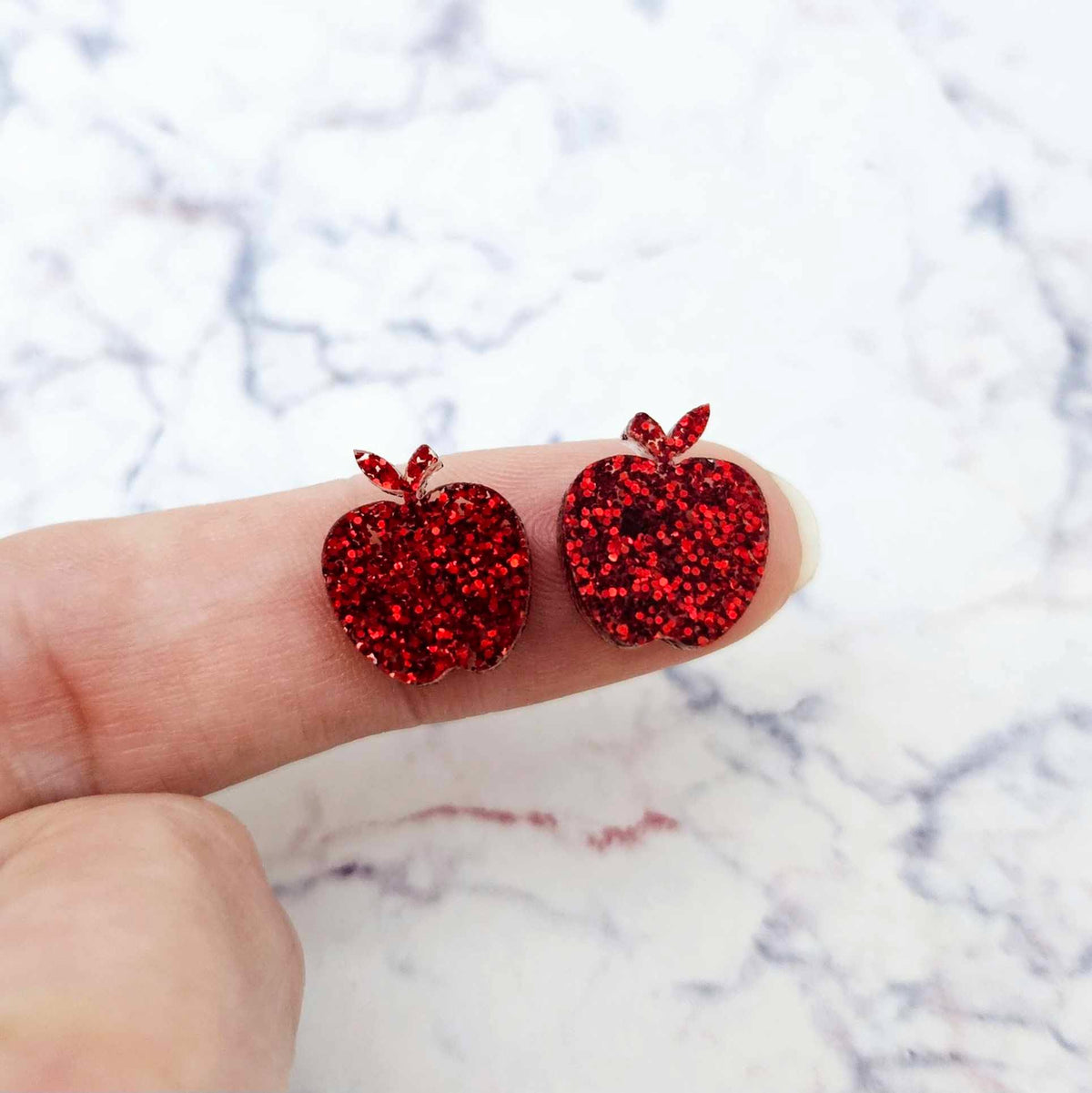 14mm red glitter acrylic apple stud earring blanks shown on a finger for size reference.