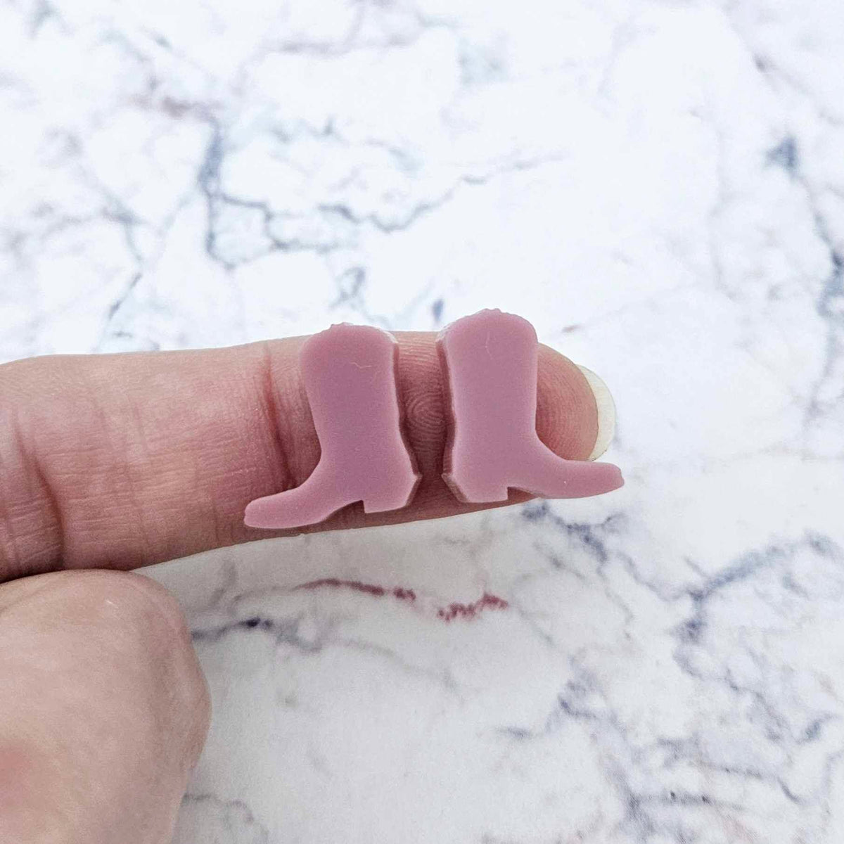 One pair of 15mm dusty rose pink acrylic boot stud earring blanks shown on a finger for size reference.