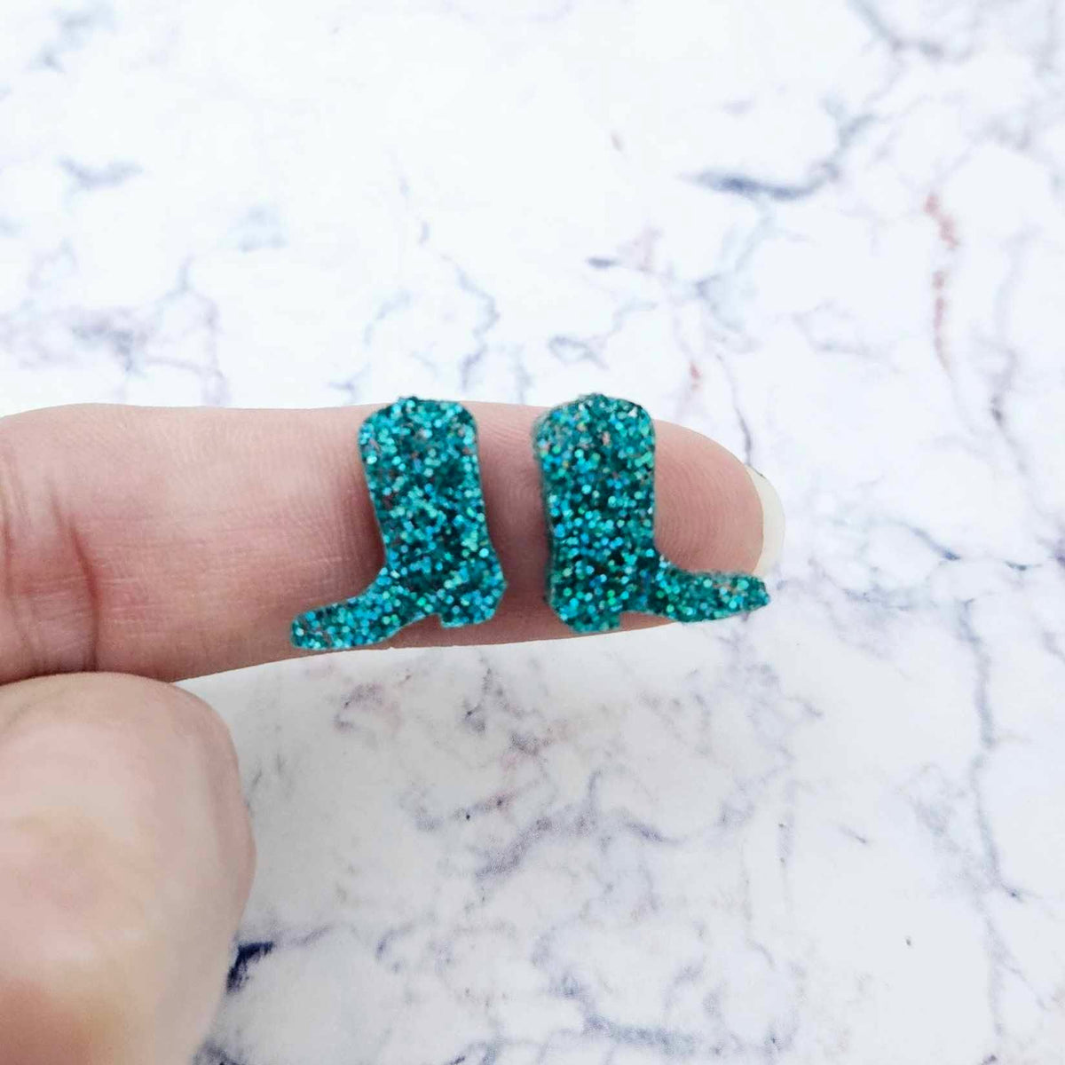 One pair of 15mm teal glitter acrylic boot stud earring blanks shown on a finger to for size reference.