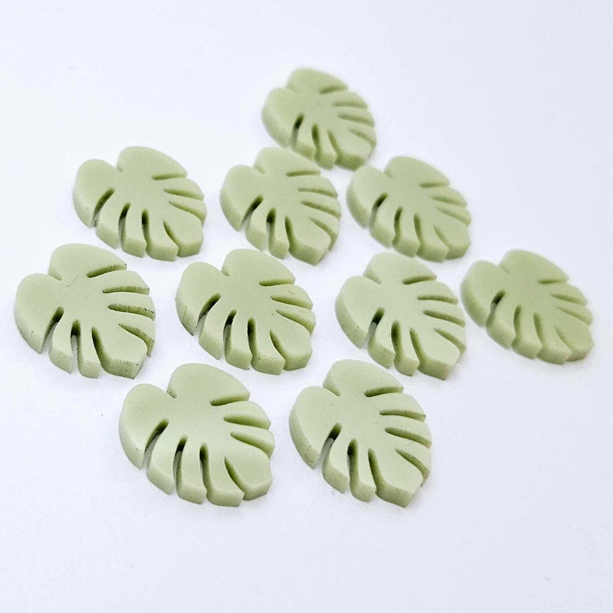 17mm eucalyptus green monstera leaf acrylic stud earring blanks laid flat together.