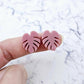 One pair of 17mm dusty rose pink acrylic monstera leaf stud earring blanks shown on a finger for size reference.