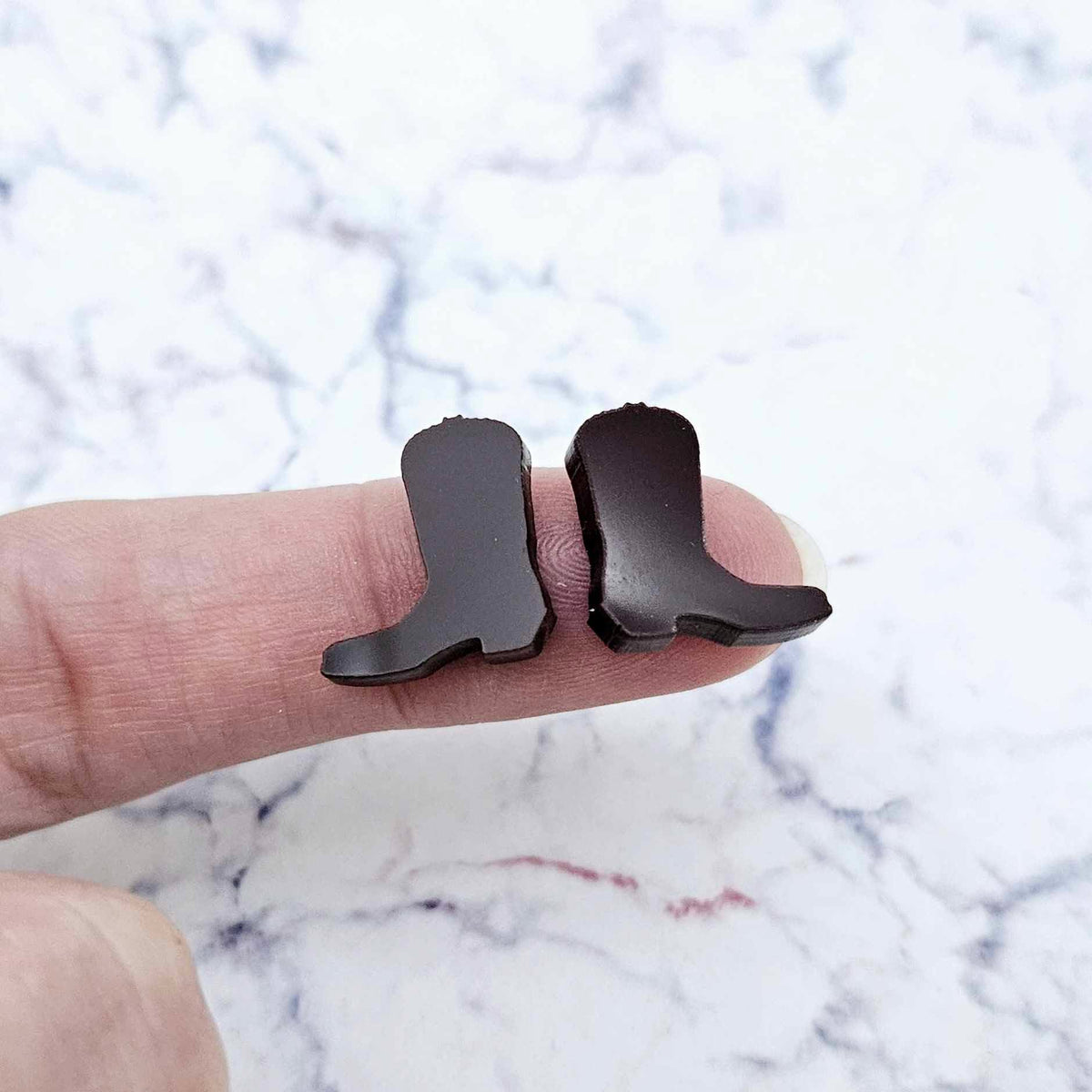 One pair of 15mm chocolate brown acrylic boot stud earring blanks shown on a finger for size reference.