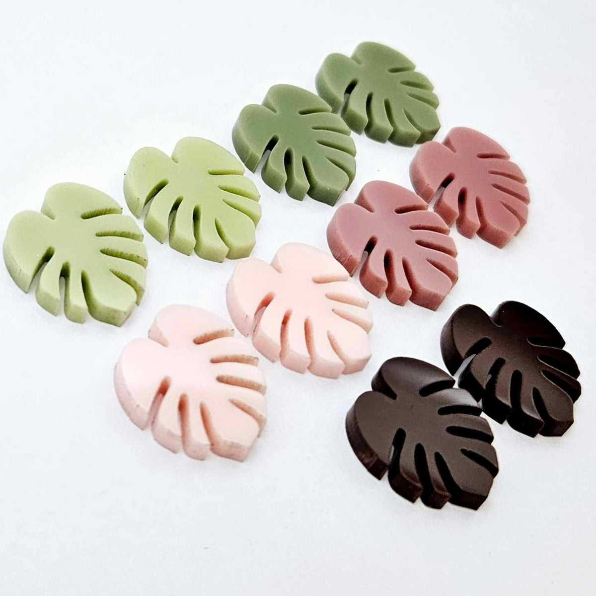 17mm monstera leaf acrylic stud earring blanks in strawberry milkshake, dusty rose, eucalyptus, olive green and chocolate brown, with one pair of each colour laid flat together.