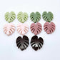 17mm monstera leaf acrylic stud earring blanks in strawberry milkshake, dusty rose, eucalyptus, olive green and chocolate brown, with one pair of each colour laid flat together.