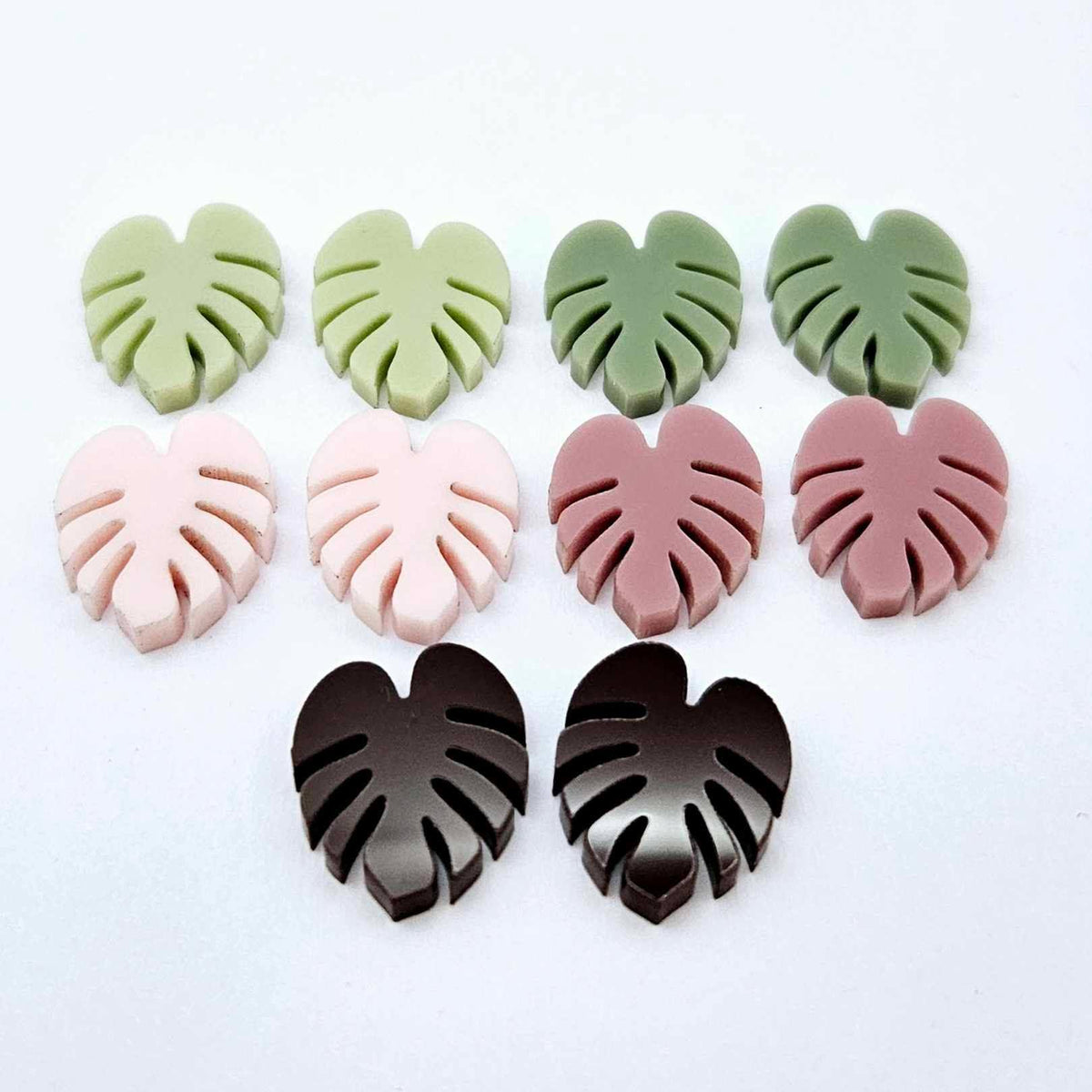 17mm monstera leaf acrylic stud earring blanks in strawberry milkshake, dusty rose, eucalyptus, olive green and chocolate brown, with one pair of each colour laid flat together.