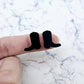 One pair of 15mm black acrylic boot stud earring blanks shown on a finger for size reference.