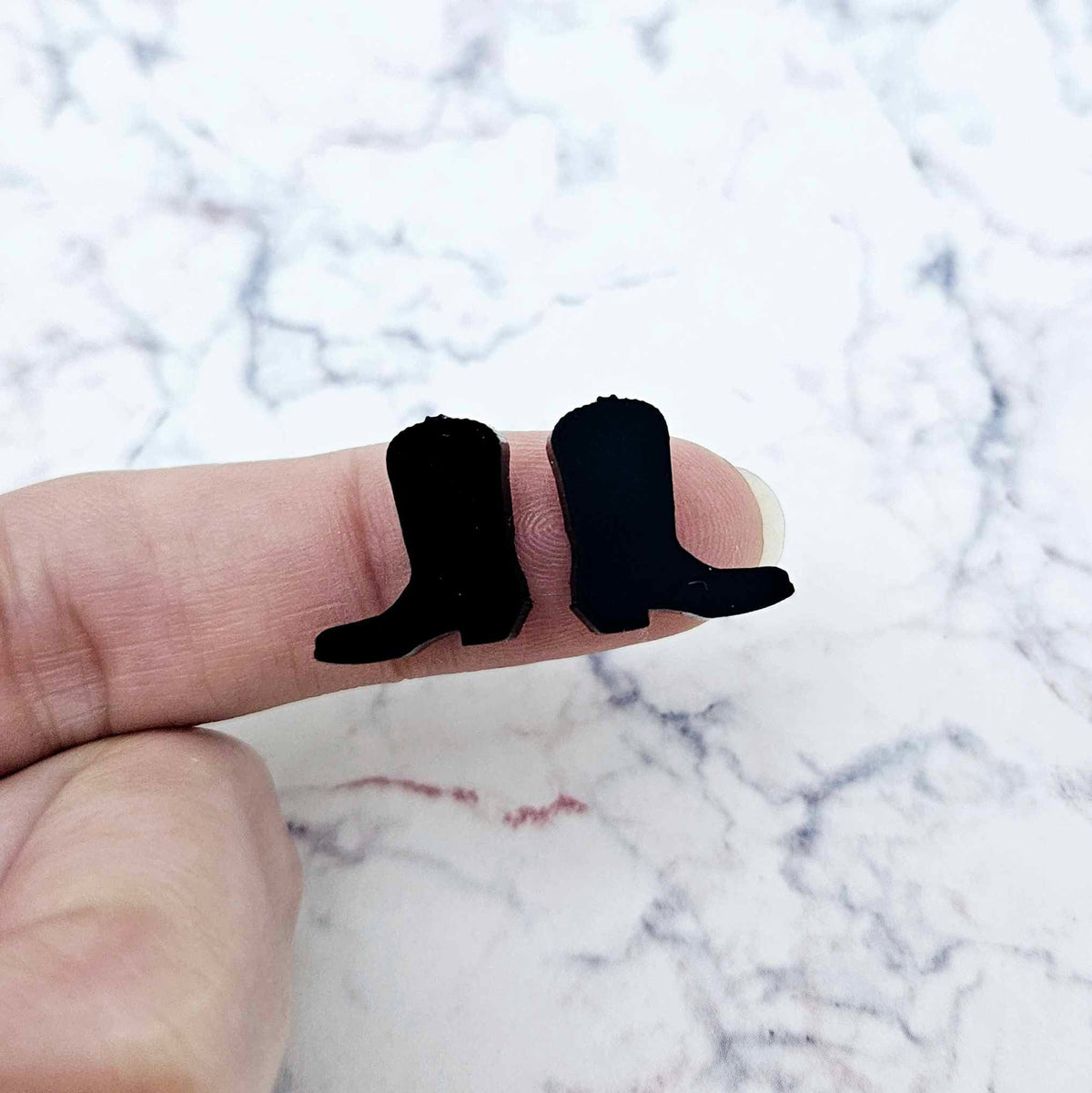 One pair of 15mm black acrylic boot stud earring blanks shown on a finger for size reference.