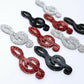 40mm glitter treble clef earring dangle blanks in silver glitter, red glitter and holographic black glitter, laid flat together.