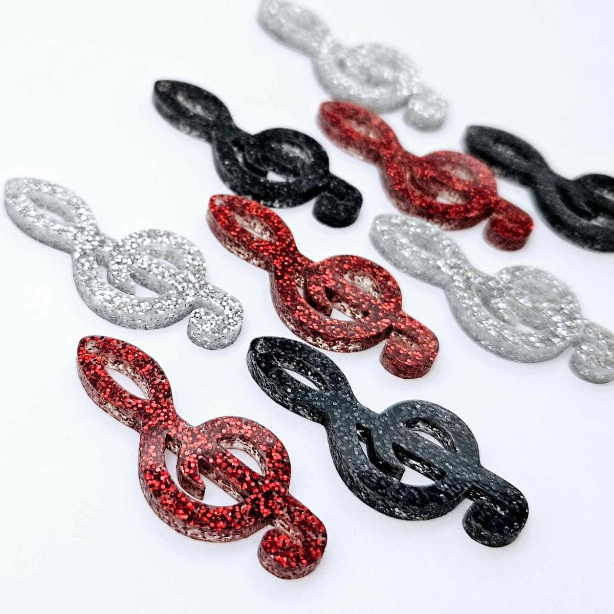 40mm glitter treble clef earring dangle blanks in silver glitter, red glitter and holographic black glitter, laid flat together.