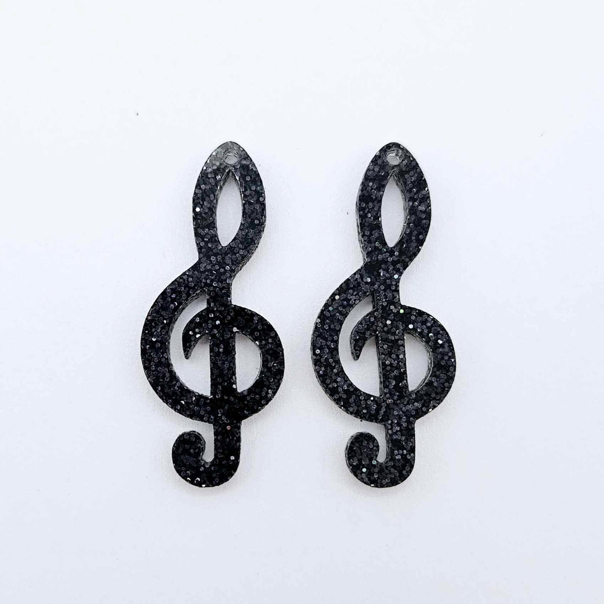 One pair of 40mm holographic black glitter acrylic treble clef earring dangle blanks laid flat.