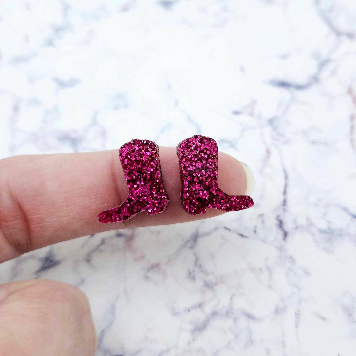 One pair of 15mm hot pink glitter acrylic boot stud earring blanks shown on a finger to for size reference.