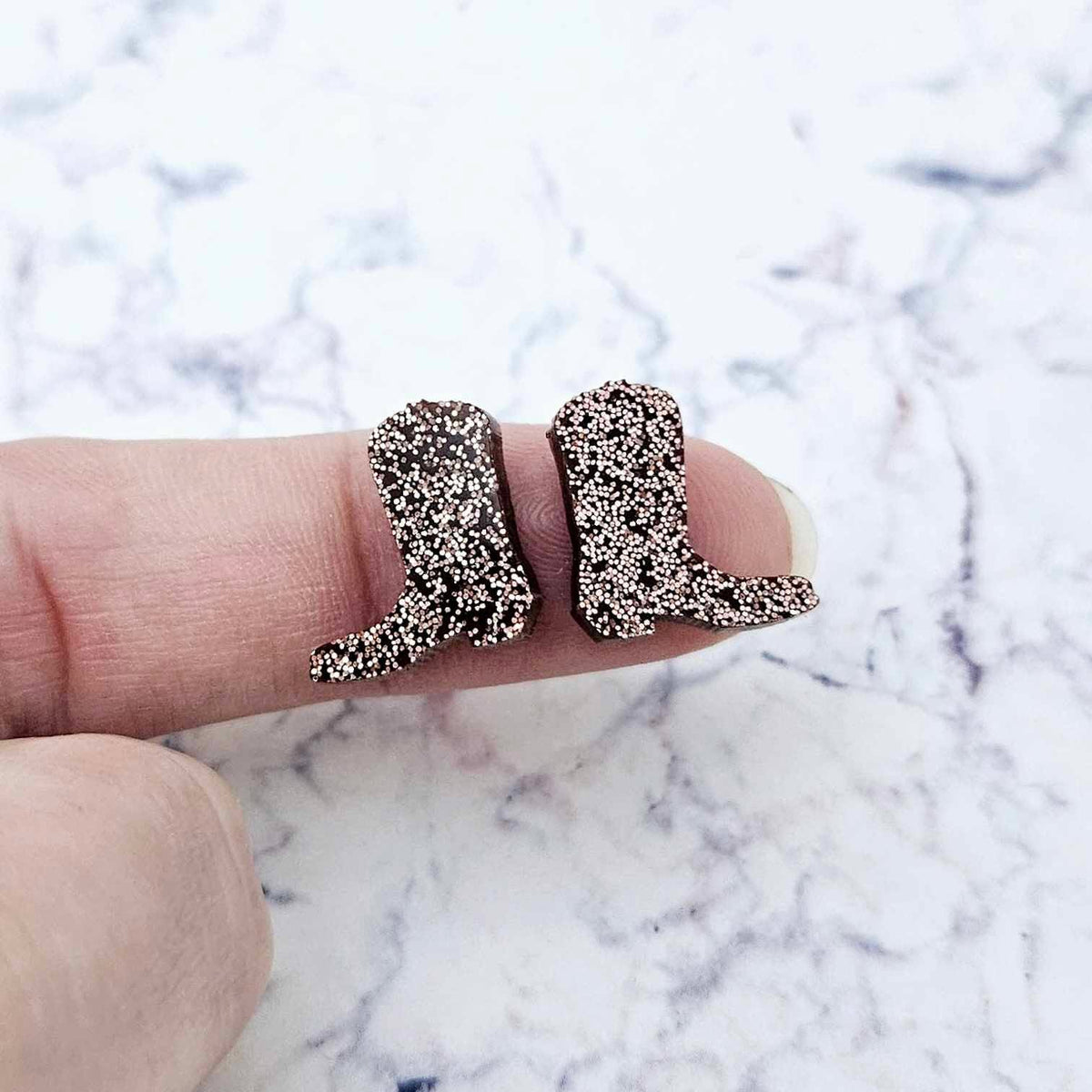 One pair of 15mm copper glitter acrylic boot stud earring blanks shown on a finger to for size reference.