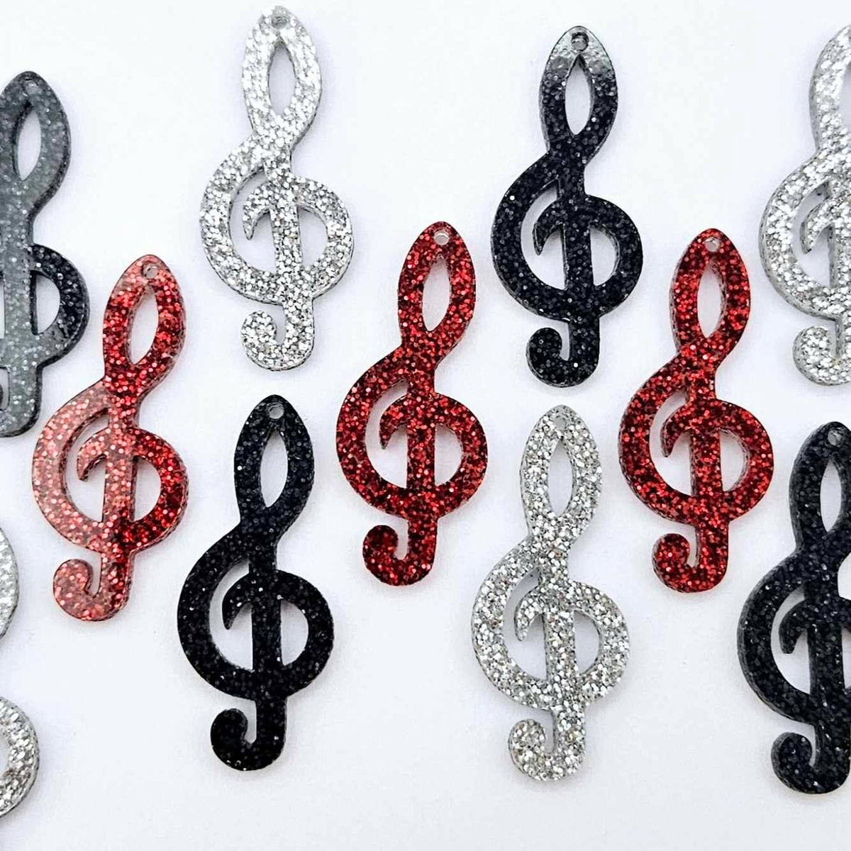 40mm glitter treble clef earring dangle blanks in silver glitter, red glitter and holographic black glitter, laid flat together.