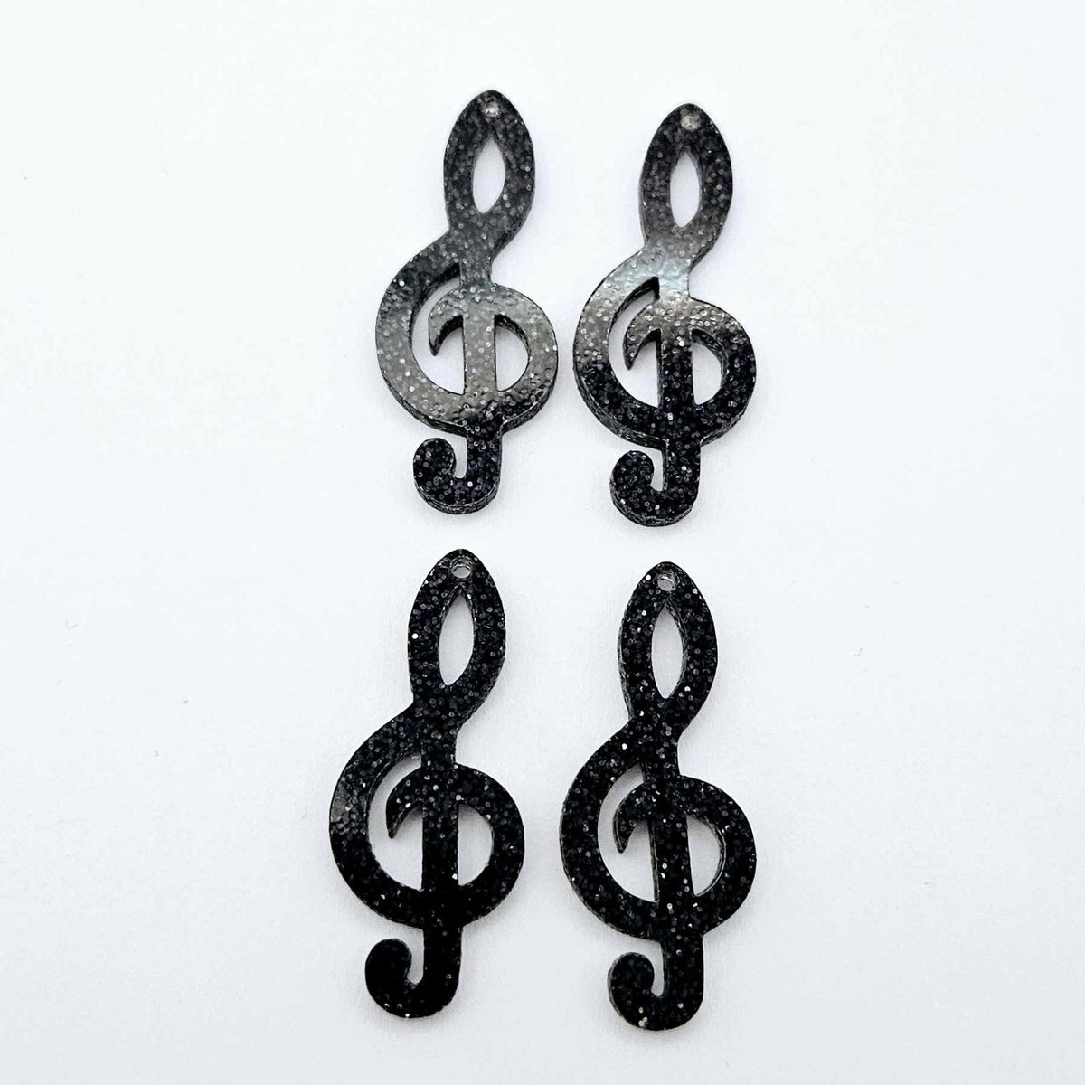 Two pairs of 40mm holographic black glitter acrylic treble clef earring dangle blanks laid flat.