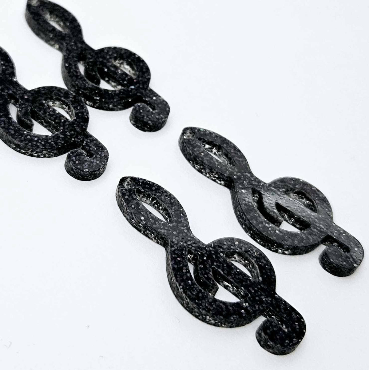 Two pairs of 40mm holographic black glitter acrylic treble clef earring dangle blanks laid flat.