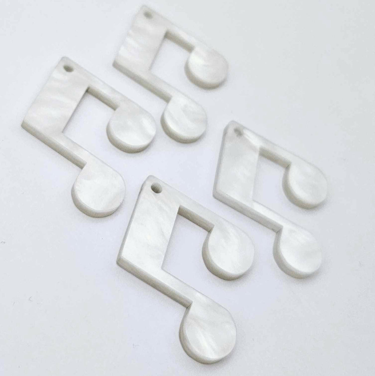 Two pairs of 35mm white marble acrylic music note earring dangle blanks laid flat together.