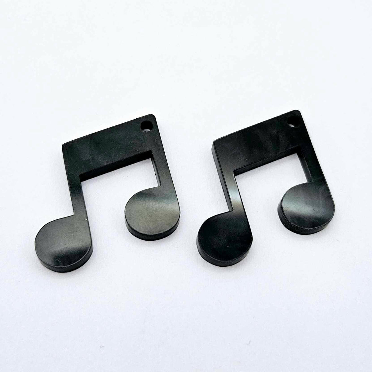 One pair of 35mm black marble acrylic music note earring dangle blanks laid flat together.