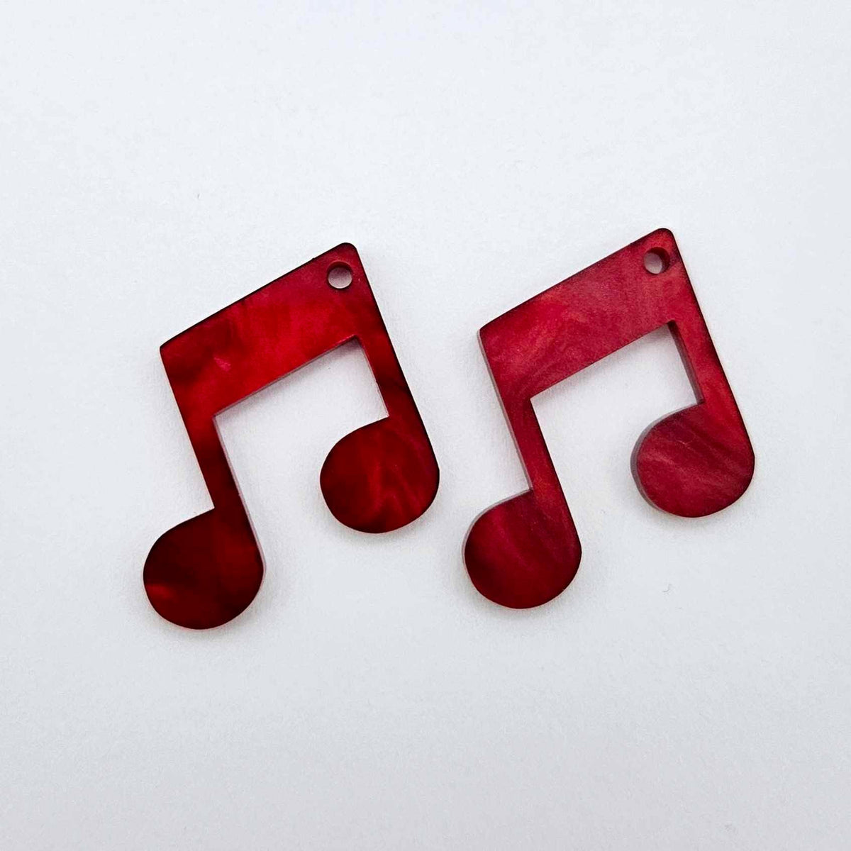 One pair of 35mm red marble acrylic music note earring dangle blanks laid flat together.