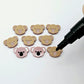 Solid Dusty Rose Pink acrylic koala stud blanks showing one finished pair with protective paper removed and engraved details paint filled in black and white, alongside unpeeled blanks with protective paper still attached and a POSCA paint pen used for decorating.