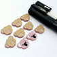 Solid Dusty Rose Pink acrylic koala stud blanks showing one finished pair with protective paper removed and engraved details paint filled in black and white, alongside unpeeled blanks with protective paper still attached and POSCA paint pens used for decorating.