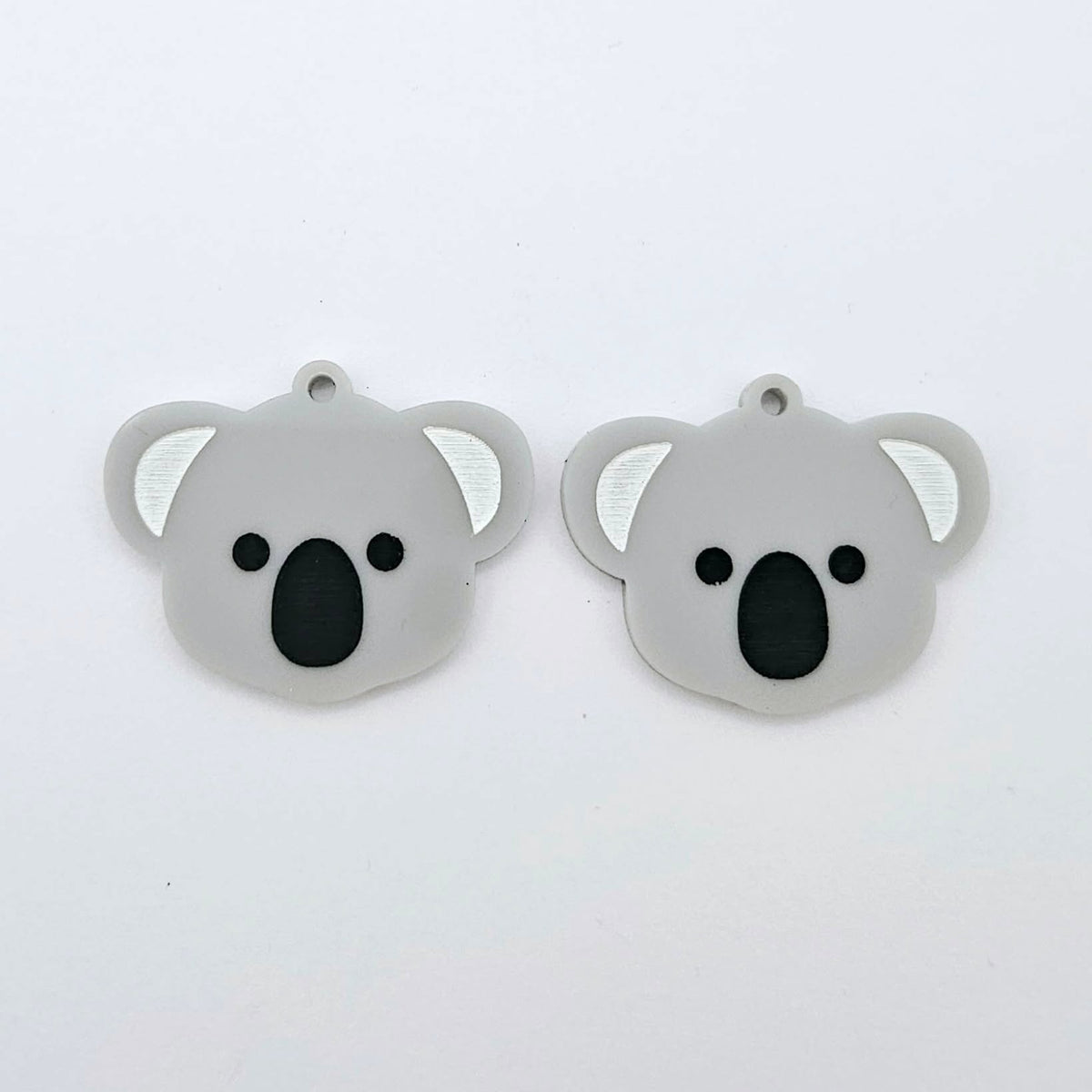 Pair of solid grey acrylic koala dangle blanks laid flat, featuring engraved eyes, nose and inner ear details paint filled with black and white for a cute Australiana earring design.