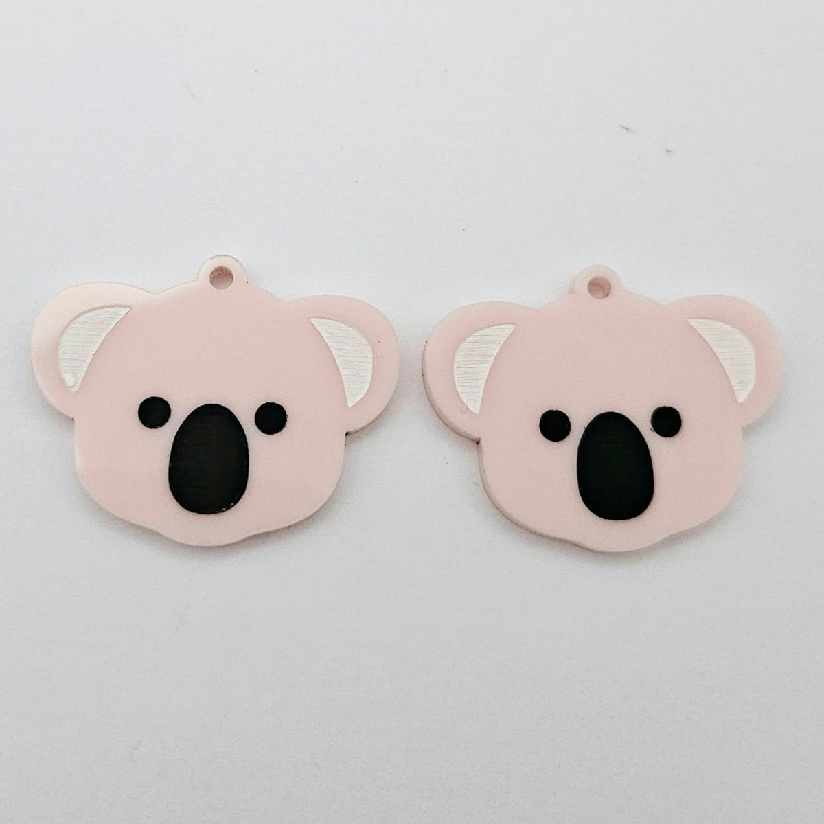 Pair of solid strawberry milkshake acrylic koala dangle blanks laid flat, featuring engraved eyes, nose and inner ear details paint filled with black and white for a cute Australiana earring design.