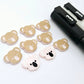 Solid Strawberry Milkshake Pink acrylic koala stud blanks showing one finished pair with protective paper removed and engraved details paint filled in black and white, alongside unpeeled blanks with protective paper still attached and POSCA paint pens used for decorating.