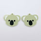 Pair of solid eucalyptus green acrylic koala dangle blanks laid flat, featuring engraved eyes, nose and inner ear details paint filled with black and white for a cute Australiana earring design.