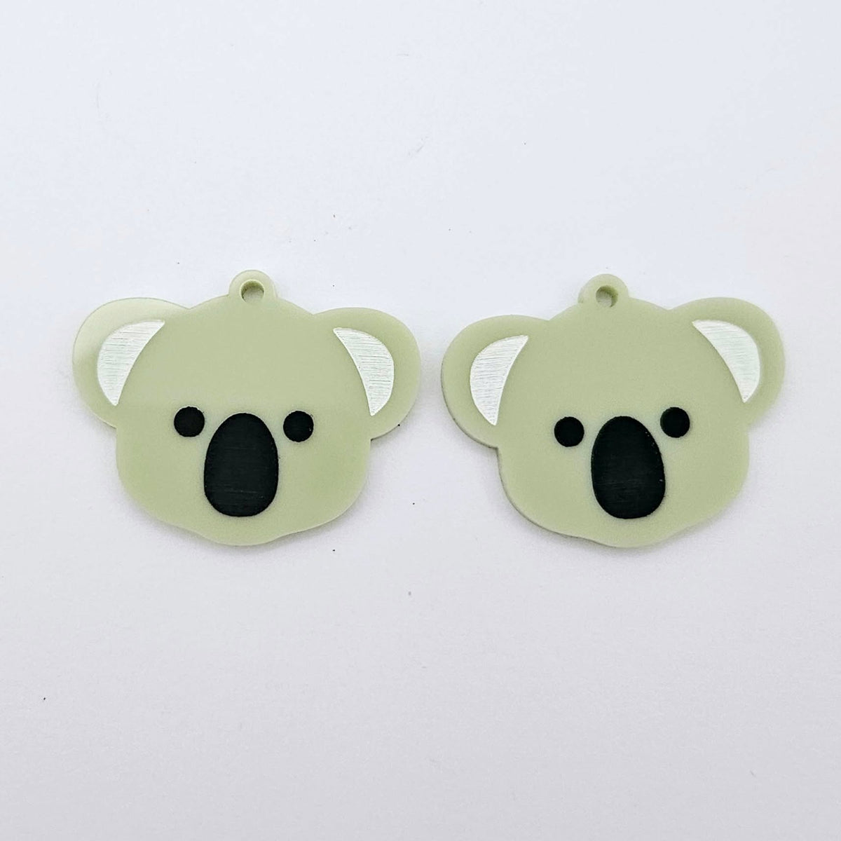 Pair of solid eucalyptus green acrylic koala dangle blanks laid flat, featuring engraved eyes, nose and inner ear details paint filled with black and white for a cute Australiana earring design.