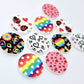 20mm UV printed Love Is Love acrylic stud earring blanks in five colourful designs: Neon Pride, Rainbow Love, Pink & Red Hearts, Black & Red Hearts and Ladybug Love, with all five pairs laid flat together.